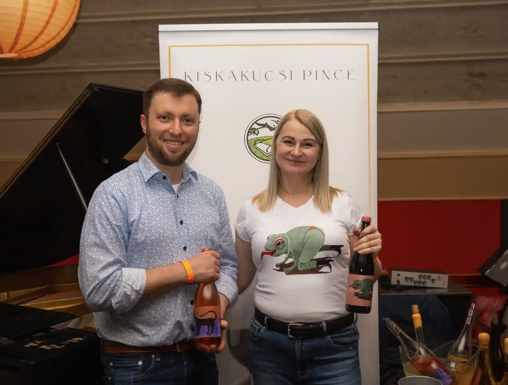 Kucsera Irén és egy férfi egy-egy palack borral a Kiskakucsi Pince molinója előtt.